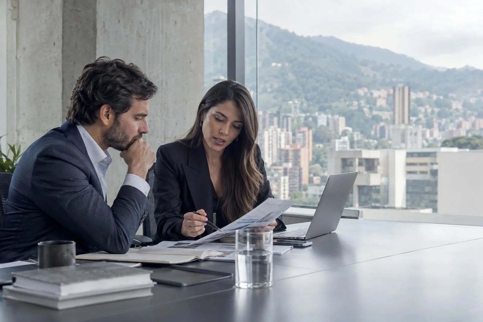 An advisor reviewing market findings with a client in an office overlooking Medellín